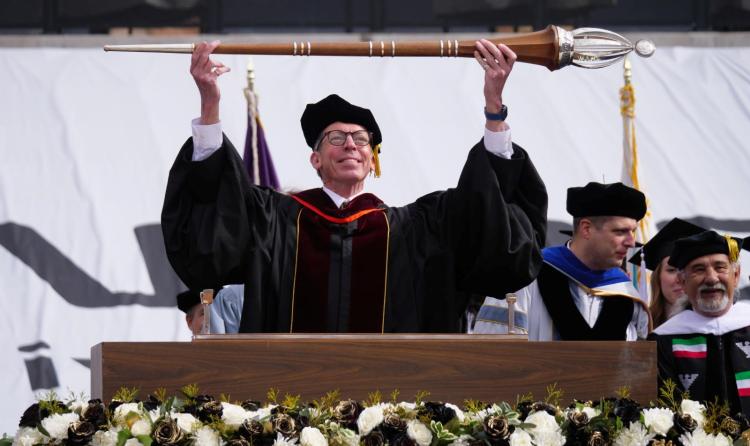 Faculty member holding scepter at graduation podium
