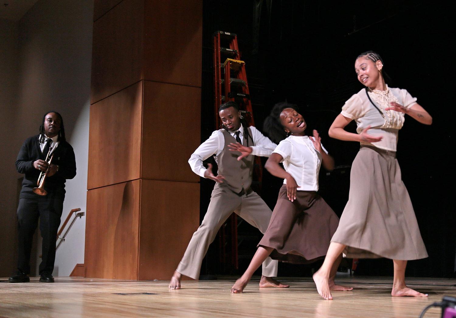 three dancers onstage with trumpet player