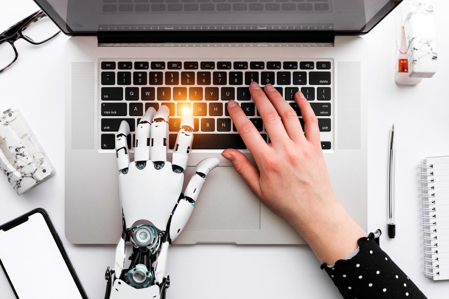 robot left hand and human right hand on laptop computer keyboard