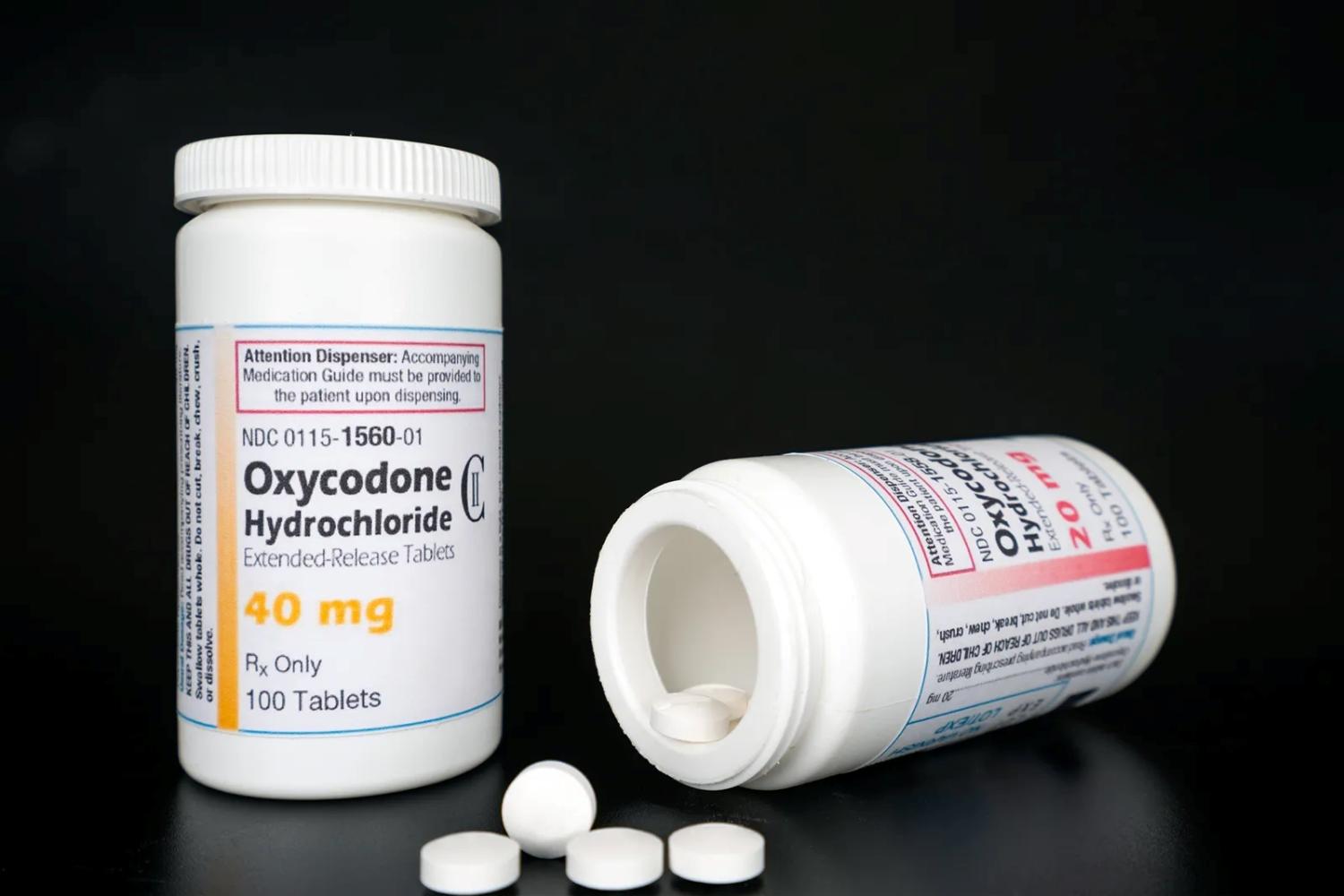 two white oxycodone bottles, one on its side with white pills spilling out