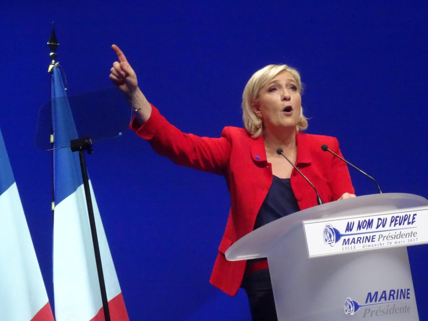Marine Le Pen speaking at podium with arm raised