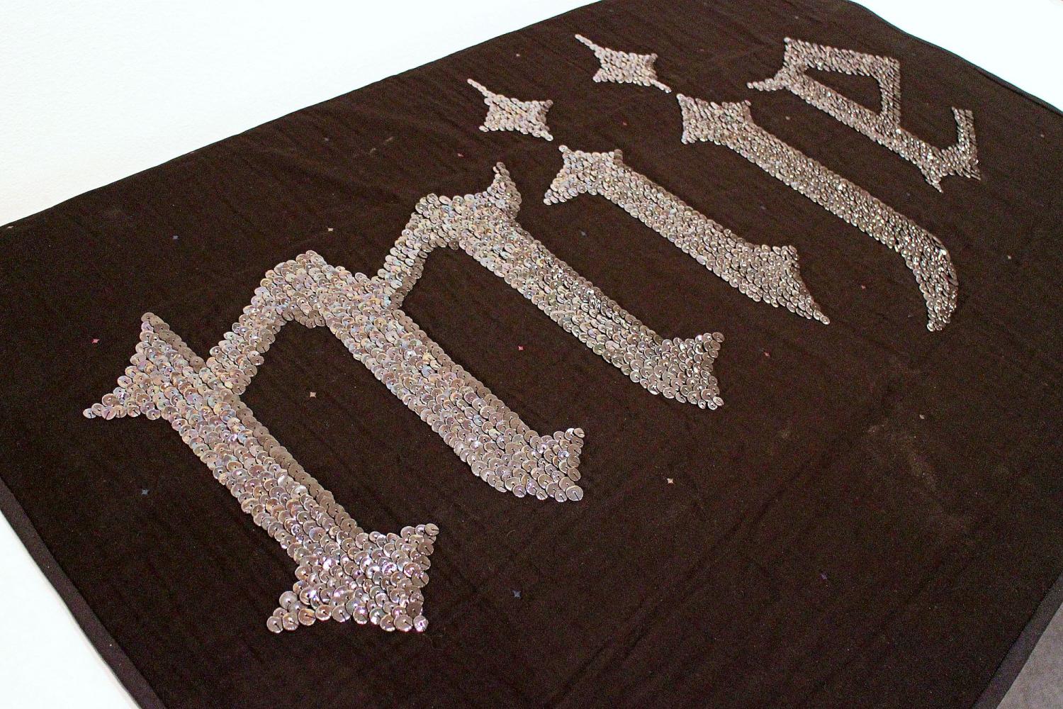 word "mije" sewn in ceramic sequins on black fabric