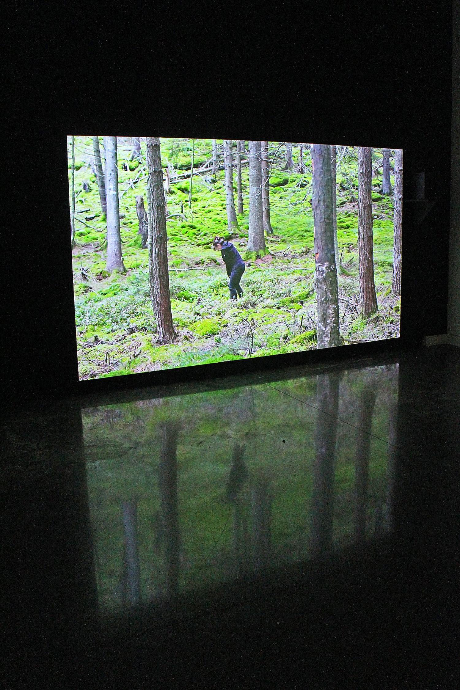 video screen showing woman wearing black clothes and digging in the woods