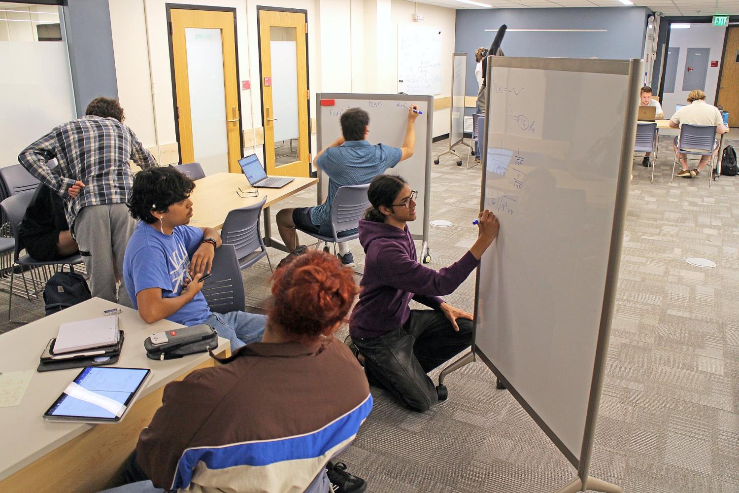 Atticus Fretz kneeling and writing on whiteboard while tutoring several students