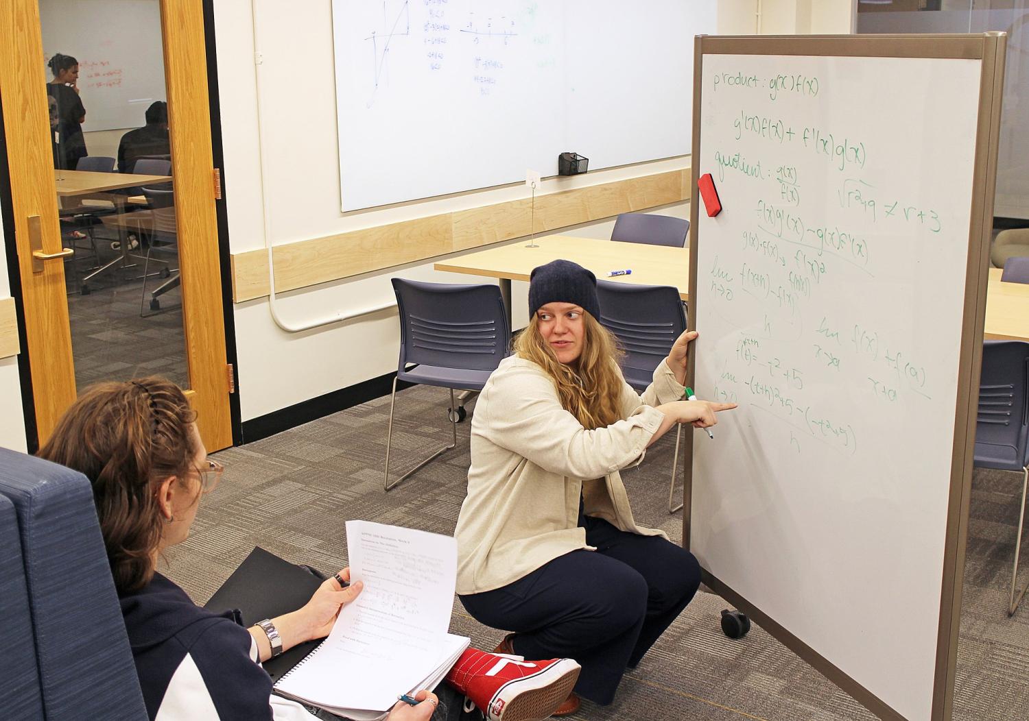 Elizabeth Wallis McGuire hunching down and pointing to math equation on whiteboard