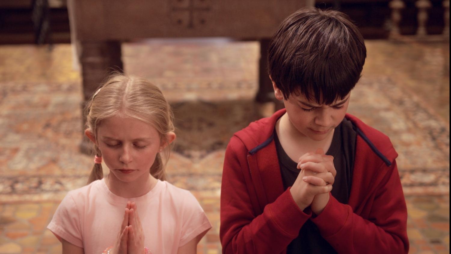 two children with eyes closed and hands clasped in prayer, in scene from short film Cherry Yogurt