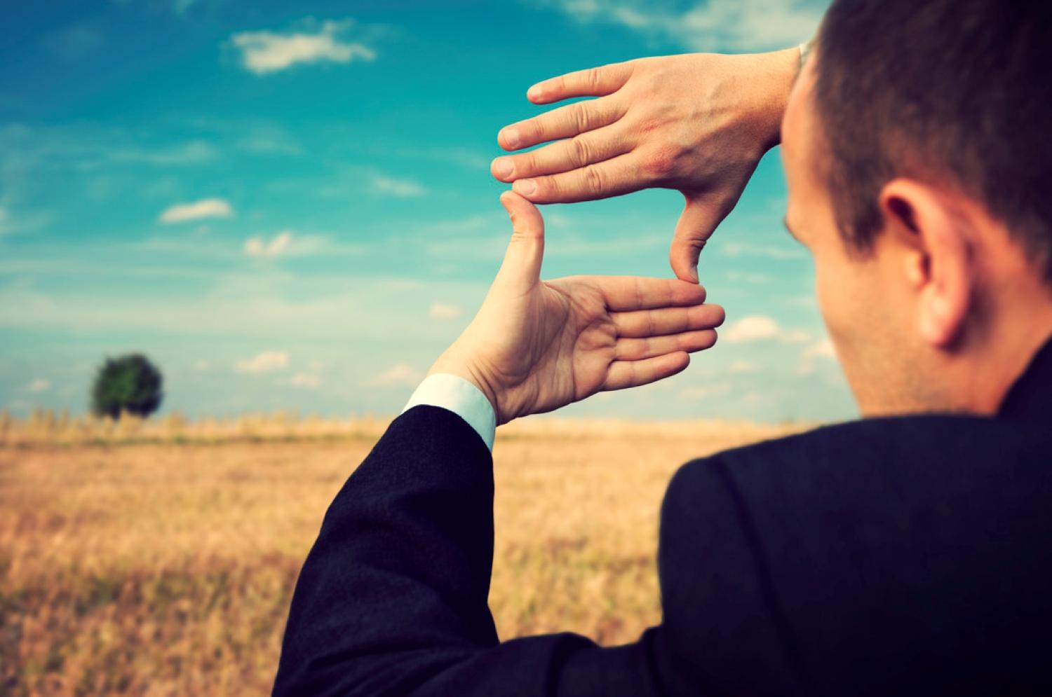 Man holding hands up to form rectangle, looking toward horizong