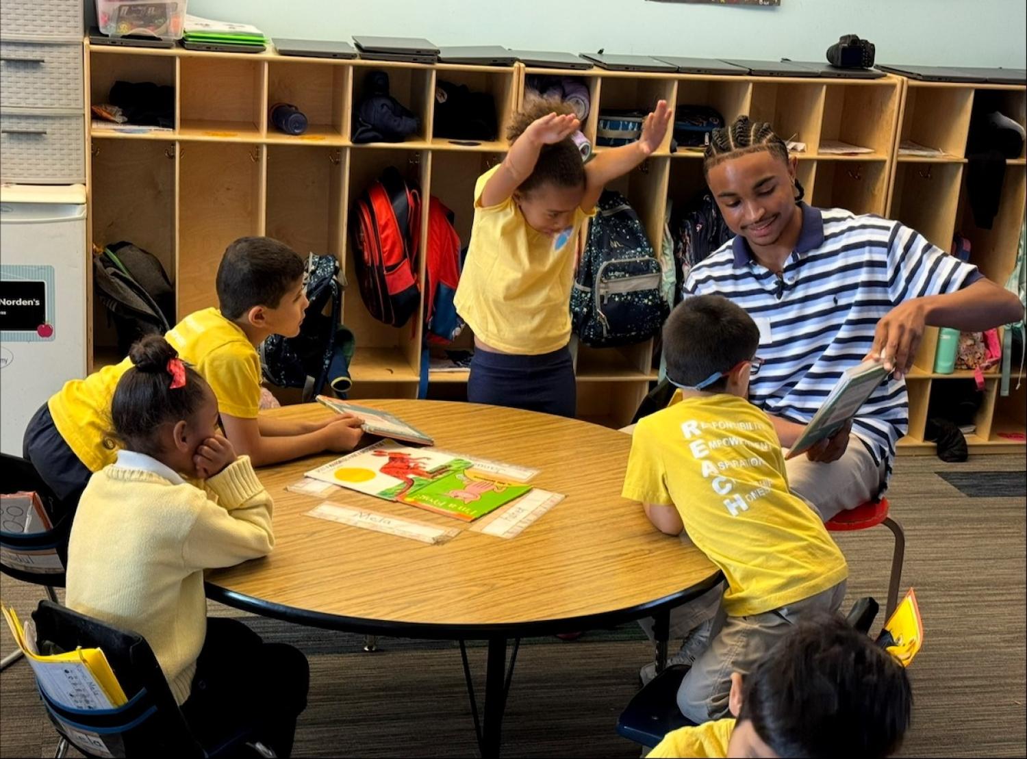 Young man reading picture book to children seated at small table