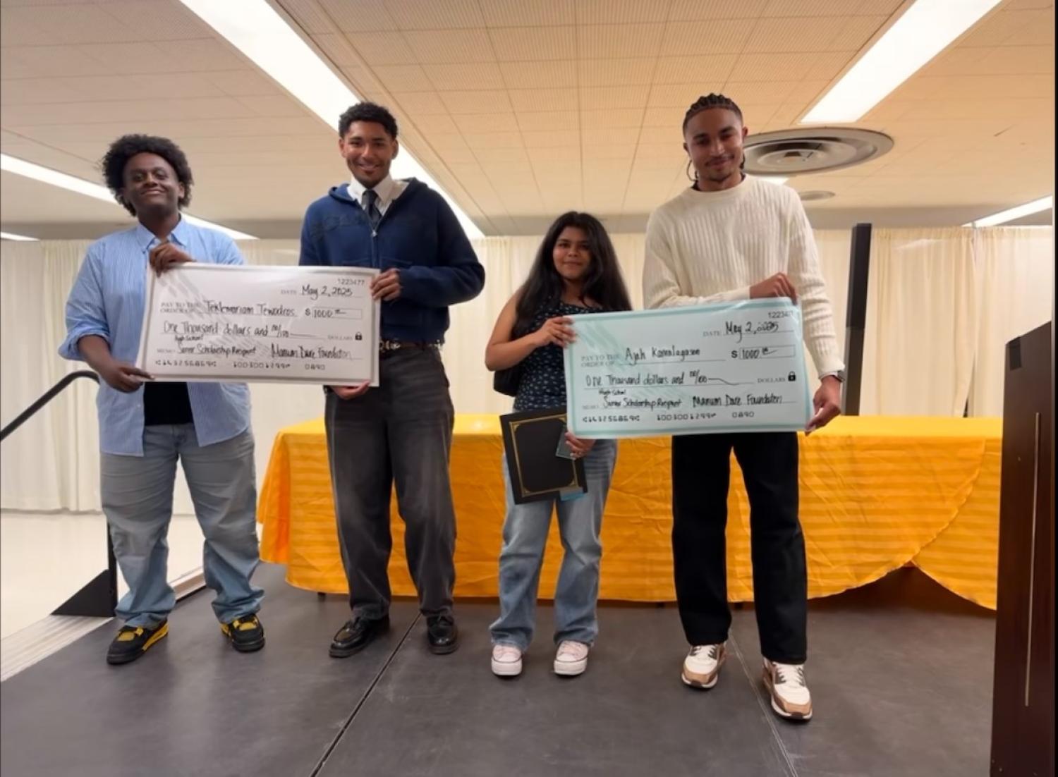 Four people standing on dais holding big checks