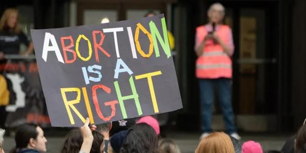 Image of a protestor holding a sign that says, "Abortion is a right"