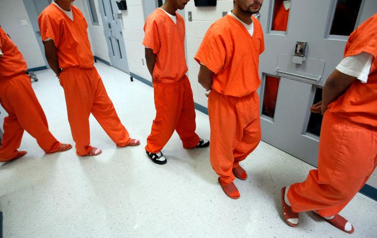Prisoners wearing orange jumpsuits in prison hallway