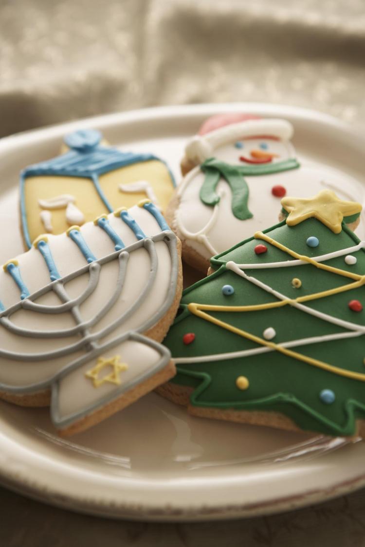 Cookies shaped like a menorah, a dreidel, a snowman and a Christmas tree sit on a plate