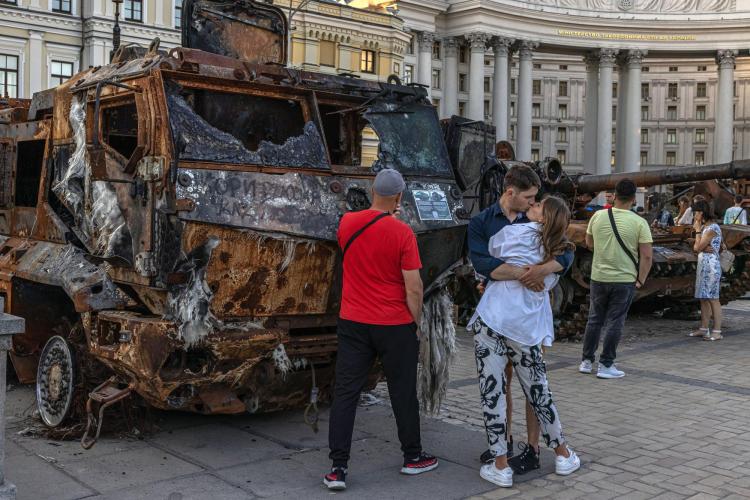 People kissing in front of a burnt out tank