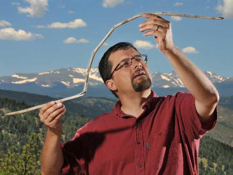 Craig Lee, of the University of Colorado Boulder, holds a 10,000-year-old atlatl dart that had been frozen in an ice sheet near Yellowstone National Park. The dart was straight when it was entombed and became bowed from the melting and barely survived being snapped in half by a passing animal. Credit Casey A. Cass/University of Colorado.