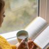 woman reading book and holding cup of coffee