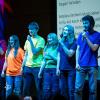 Seven students performing onstage wearing colorful T-shirts