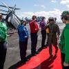 Stephen Koehler in green flight suit saluting U.S. Navy personnel on ship deck