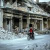 man riding bike on Syrian street bombed during war