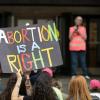 Image of a protestor holding a sign that says, "Abortion is a right"