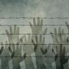 Hands behind a barbed wire fence