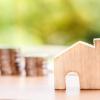 A small outline of a house with stacked coins in the background