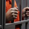 Man in orange jumpsuit holding prison bars
