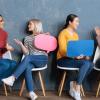 Four women holding paper conversation bubbles and talking