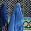 women in blue burqas walking past a colorfully tiled wall