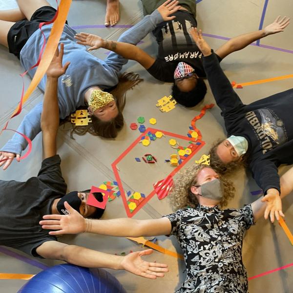 Students holding hands in a circle laying down