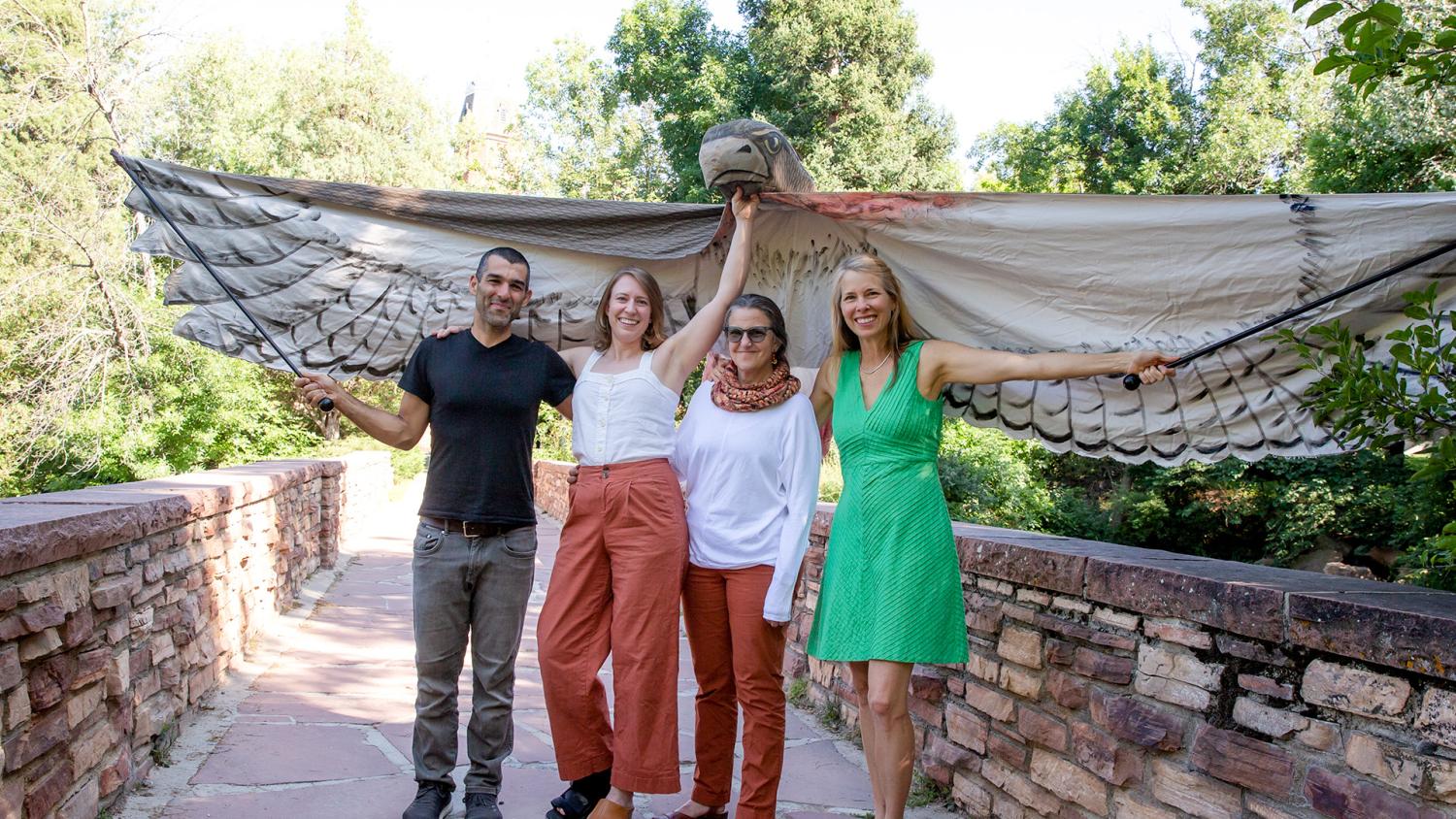 The four-person Side by Side project leadership team grinning while holding a giant youth made bird costume above their heads, with wings extended out beyond either side of them. From left to right: Drs. Shawhin Roudbari, Chelsea Hackett, Rebecca Safran, and Beth Osnes.