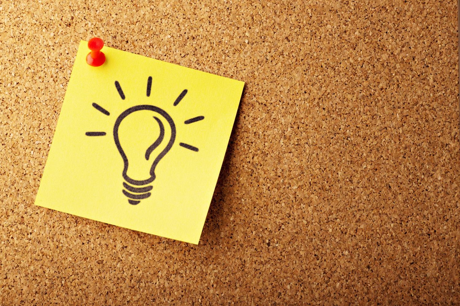 a yellow sticky note with a lightbulb drawn on it hangs from a cork board