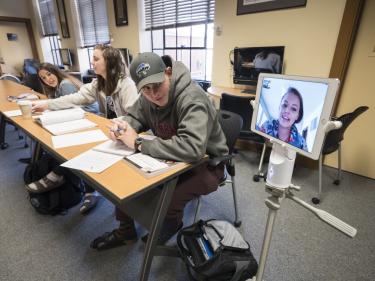 Students in conference room-style classroom, with one student on the Kubi.