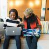 Three smiling women, one white and two Black, sitting on a sofa looking at laptops.