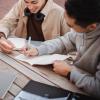 two students collaborate together with their computers and notebooks
