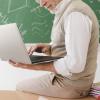 Teacher working on a laptop in front of a chalkboard with written equations