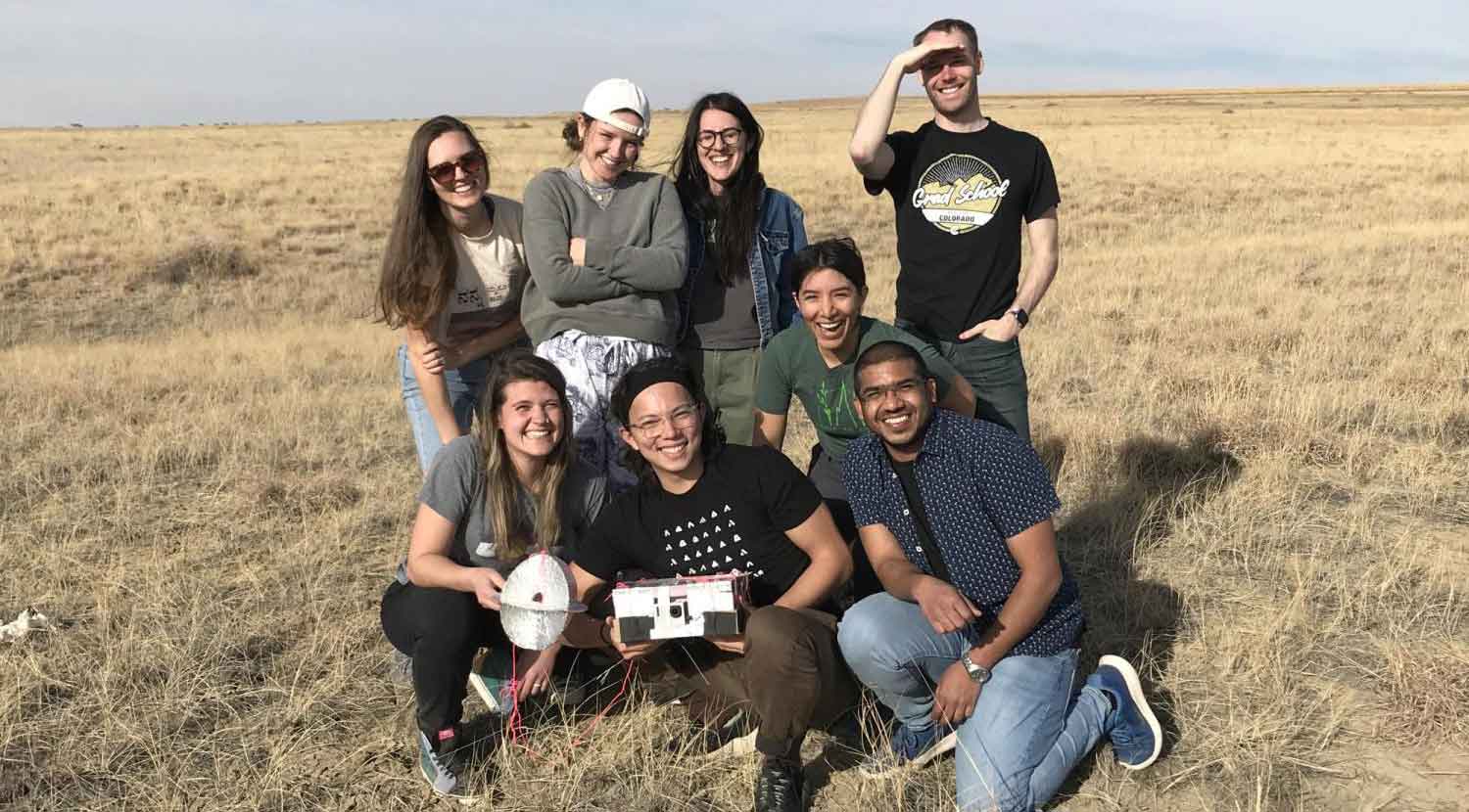 students pose in field with flight control unit