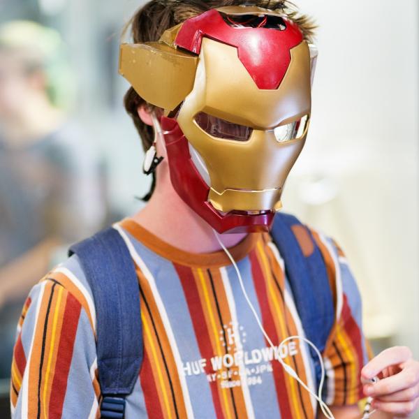 Person wearing Iron Man mask with Apple wired headphones on