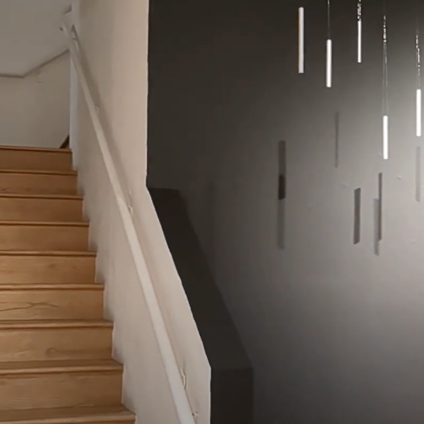 A set of stairs next to a gray wall. The gray wall is lit with a spotlight and features several metal cylinders hanging from the ceiling.