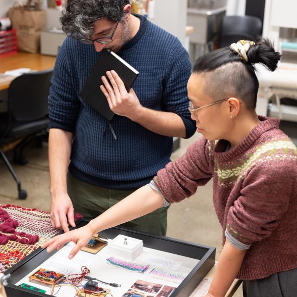 PhD student showing a guest various experimental woven forms on a table