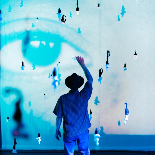 person with hat reaching up to hold a hanging sculpture in a projected environment