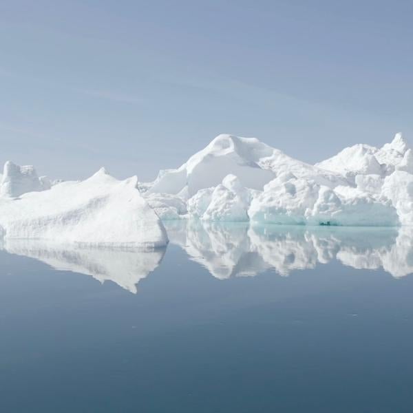 white icebergs floating in a pale blue sea white the sky almost the same color as the sea