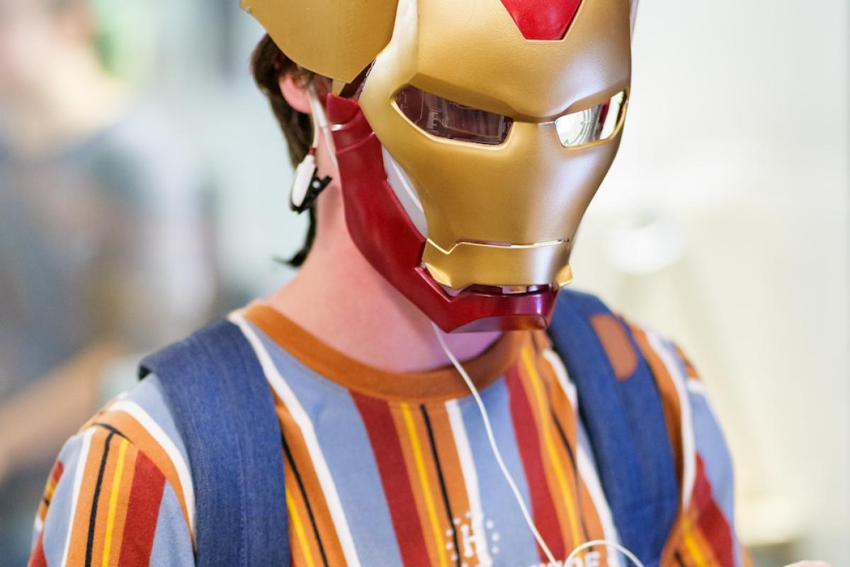 Person wearing Iron Man mask with Apple wired headphones on