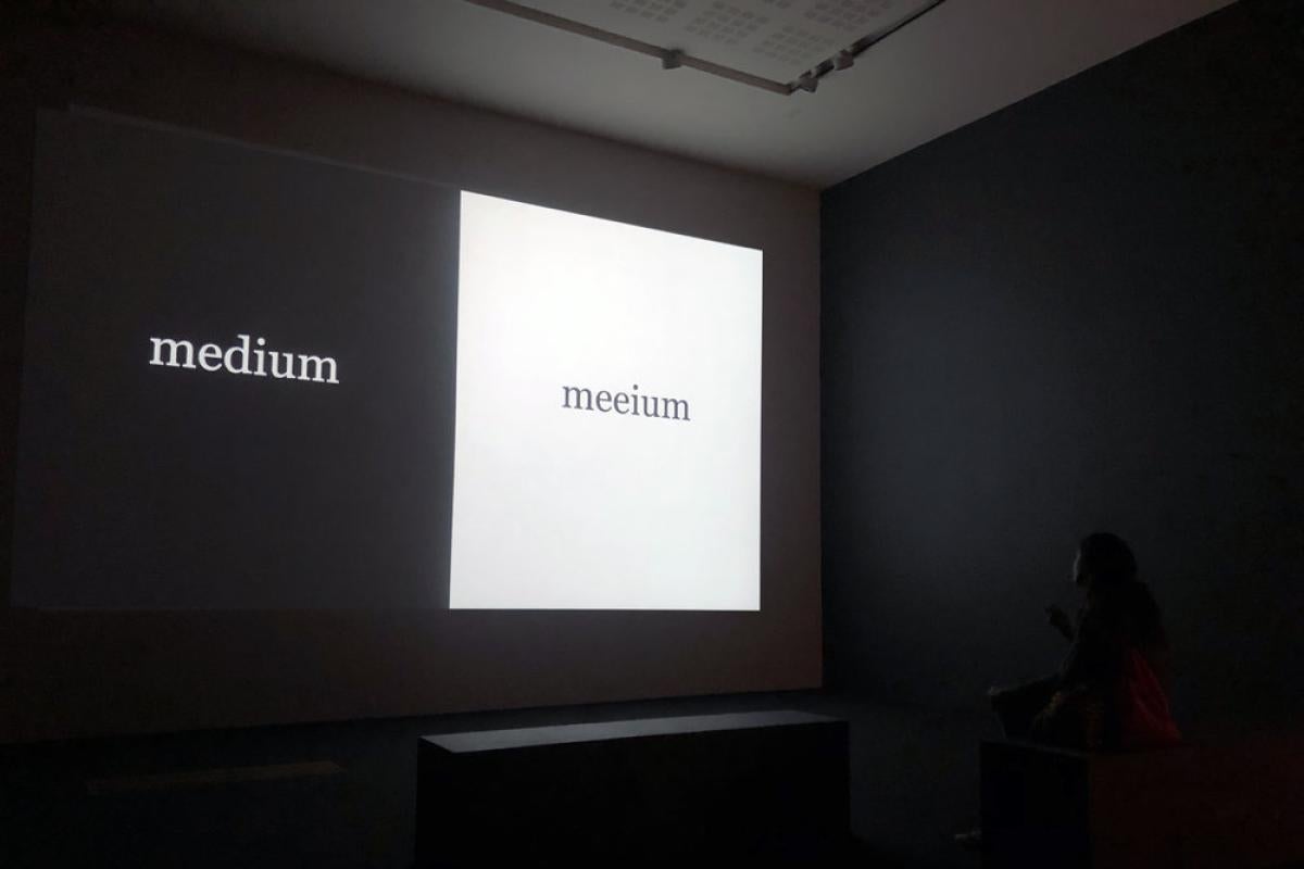 Dark room with two squares projected onto the wall- one is black with the white text medium and one is white with the black text meeium