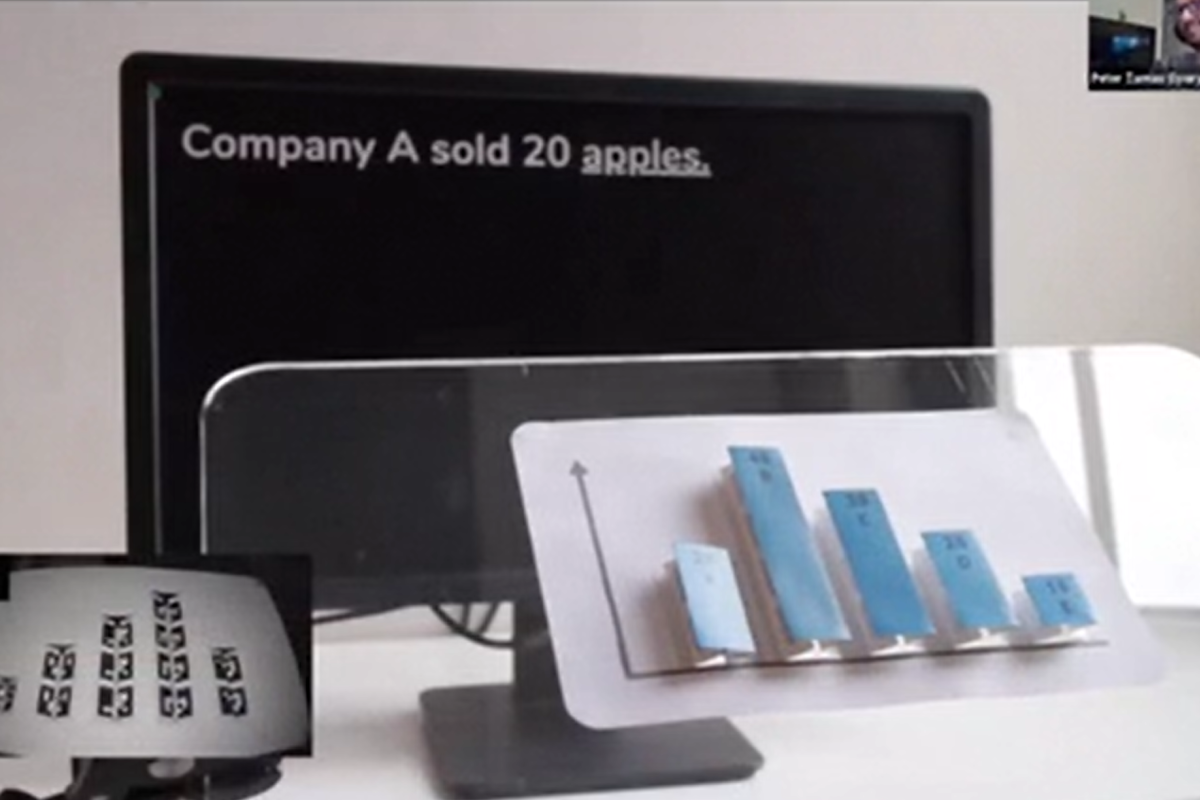 A desktop monitor; black with white text that reads "Company A sold 20 apples". In front of it is a physical model of a bar chart.
