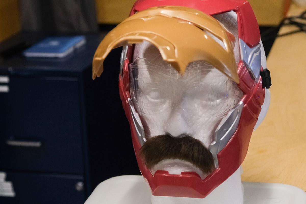 A mannequin head with a fake mustache wearing an open Ironman mask.