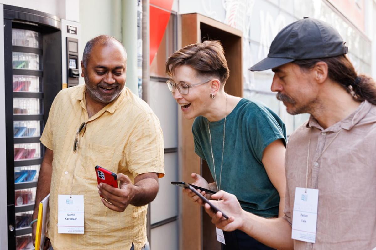 Three people looking down at their phones, smiling