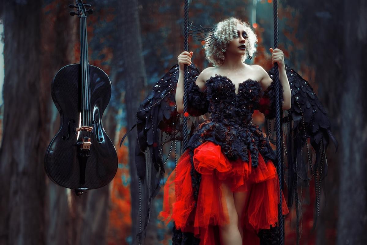 A woman in elaborate black and red garb with wings stands on a wooden swing as a black cello hovers to her right