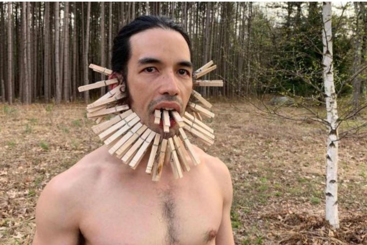 man with clothes pins framing face and attached to tongue