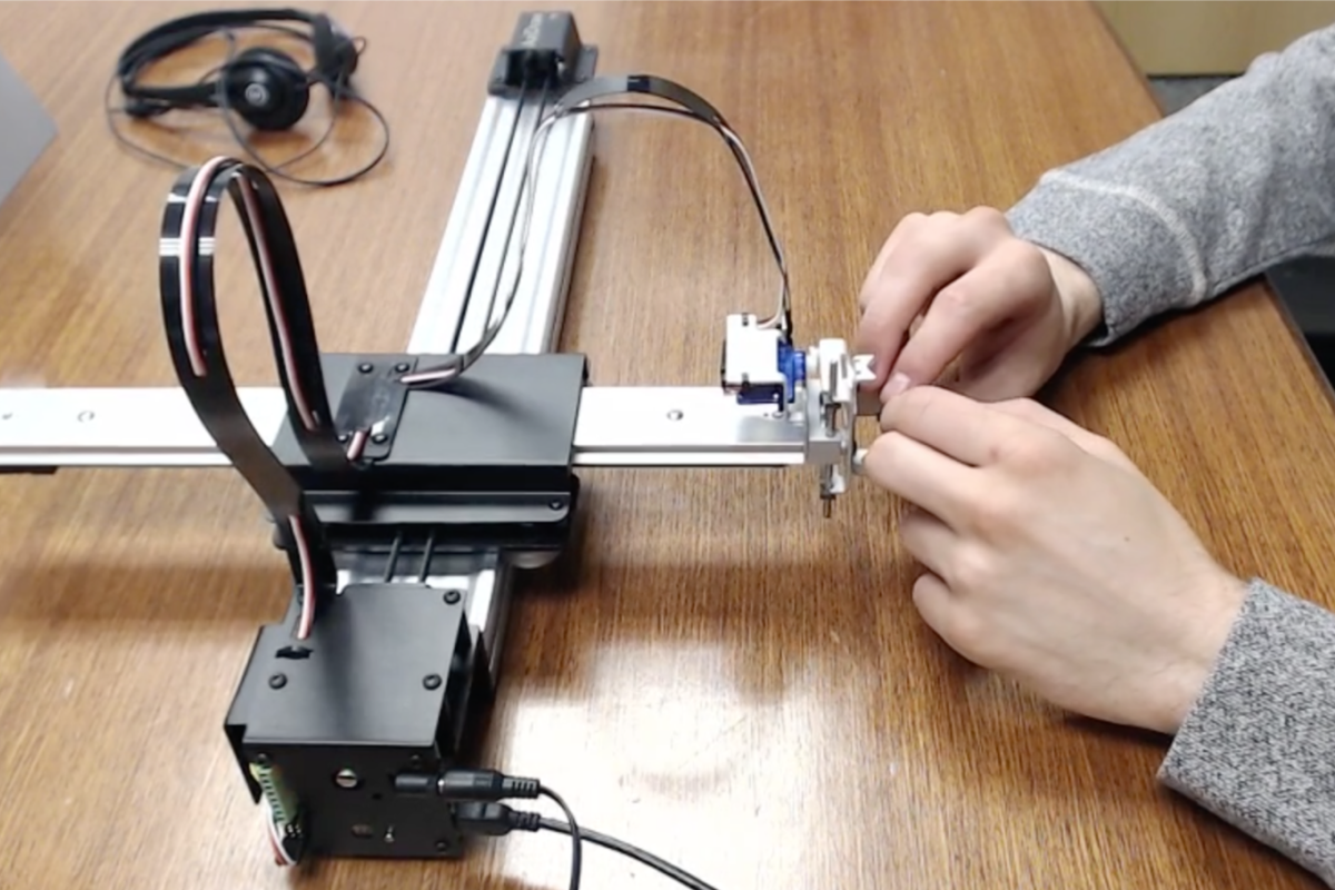 A user gripping the mechanical arm of a pen plotter to experience kinetic content.
