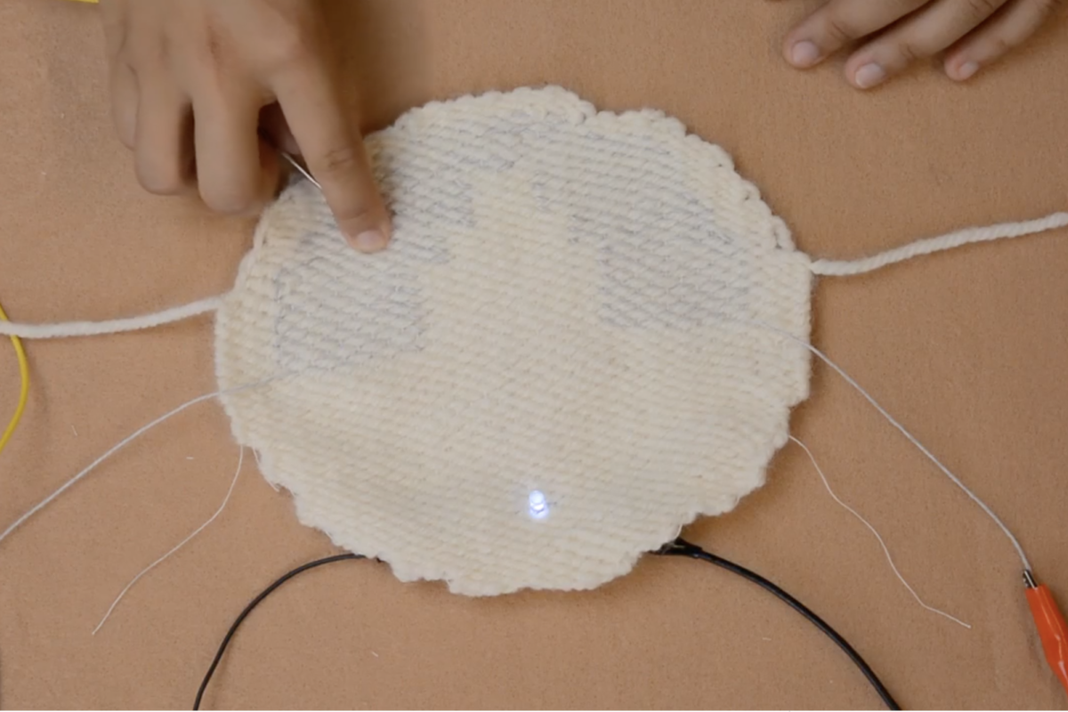 A smart fabric being touched, causing an LED light to turn on.